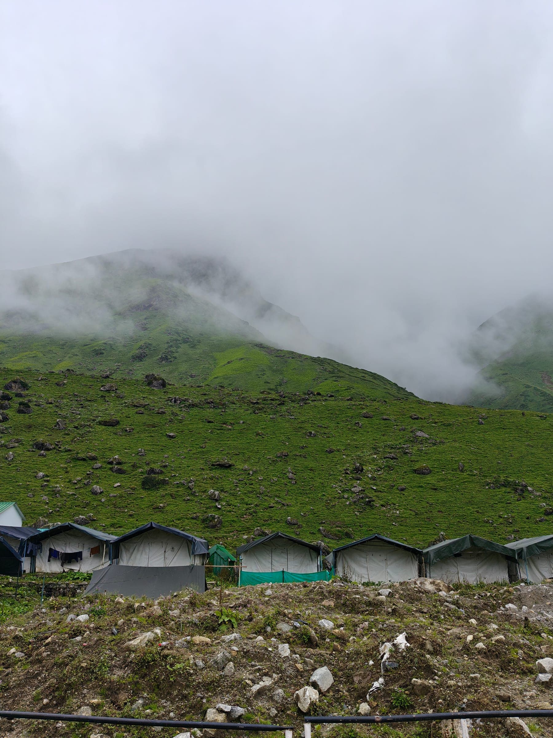 A row of canvas tents below a green slope, the mountain above lost in cloud.