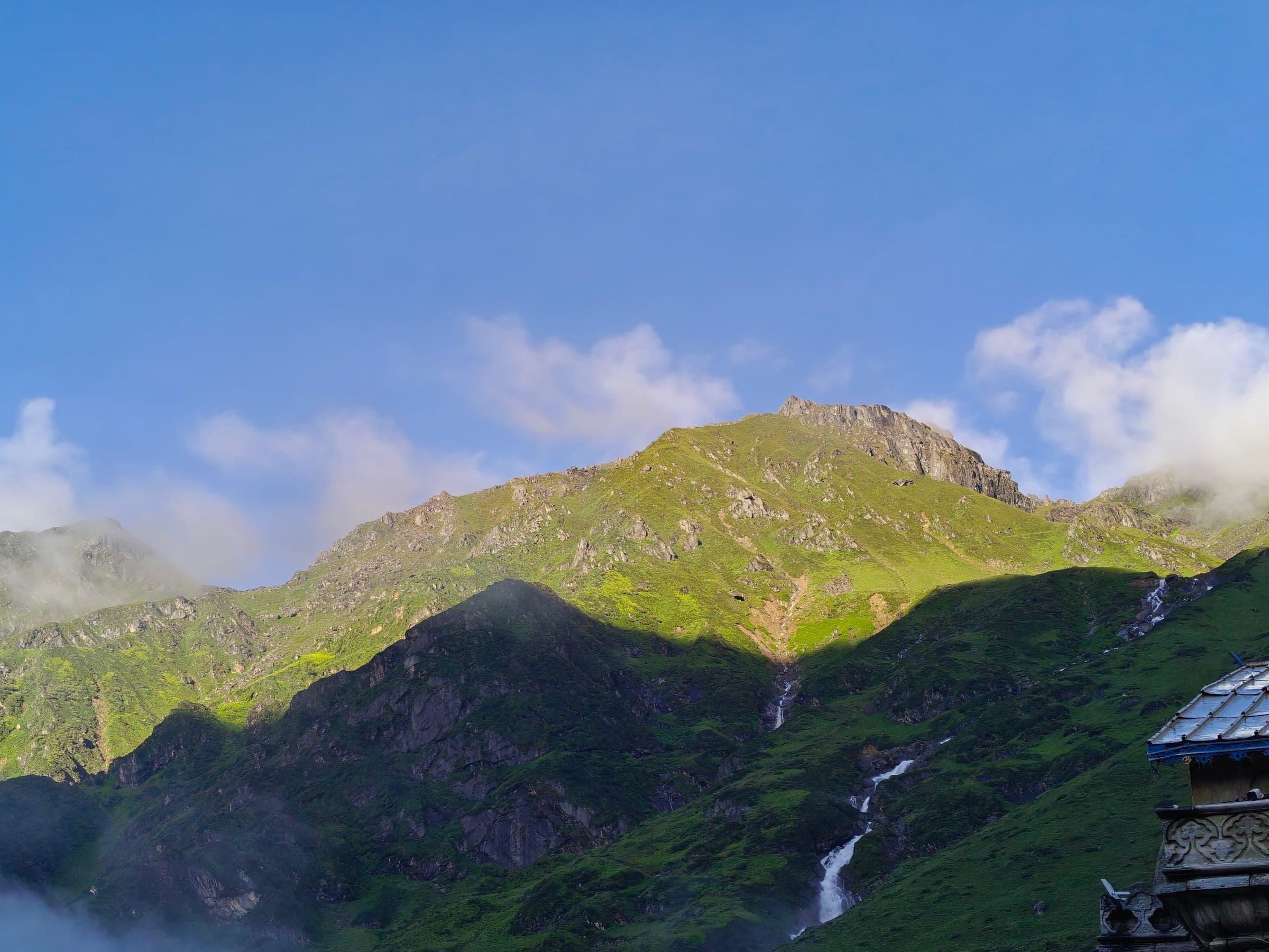 Sun on a green ridge with a waterfall running down it, the carved roof of a temple in the corner.