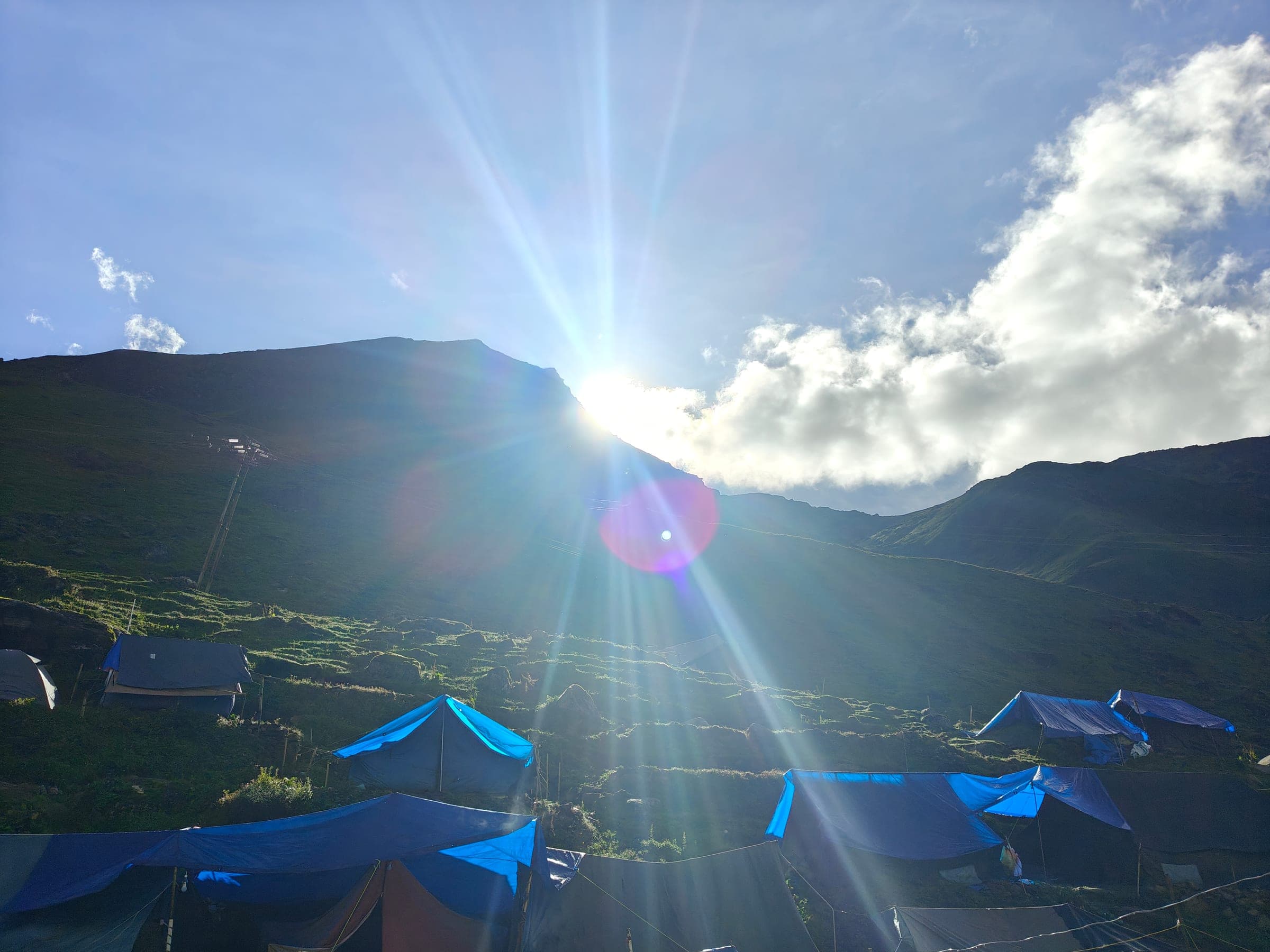 The sun bursting over a ridge above a camp of blue tarpaulin tents.