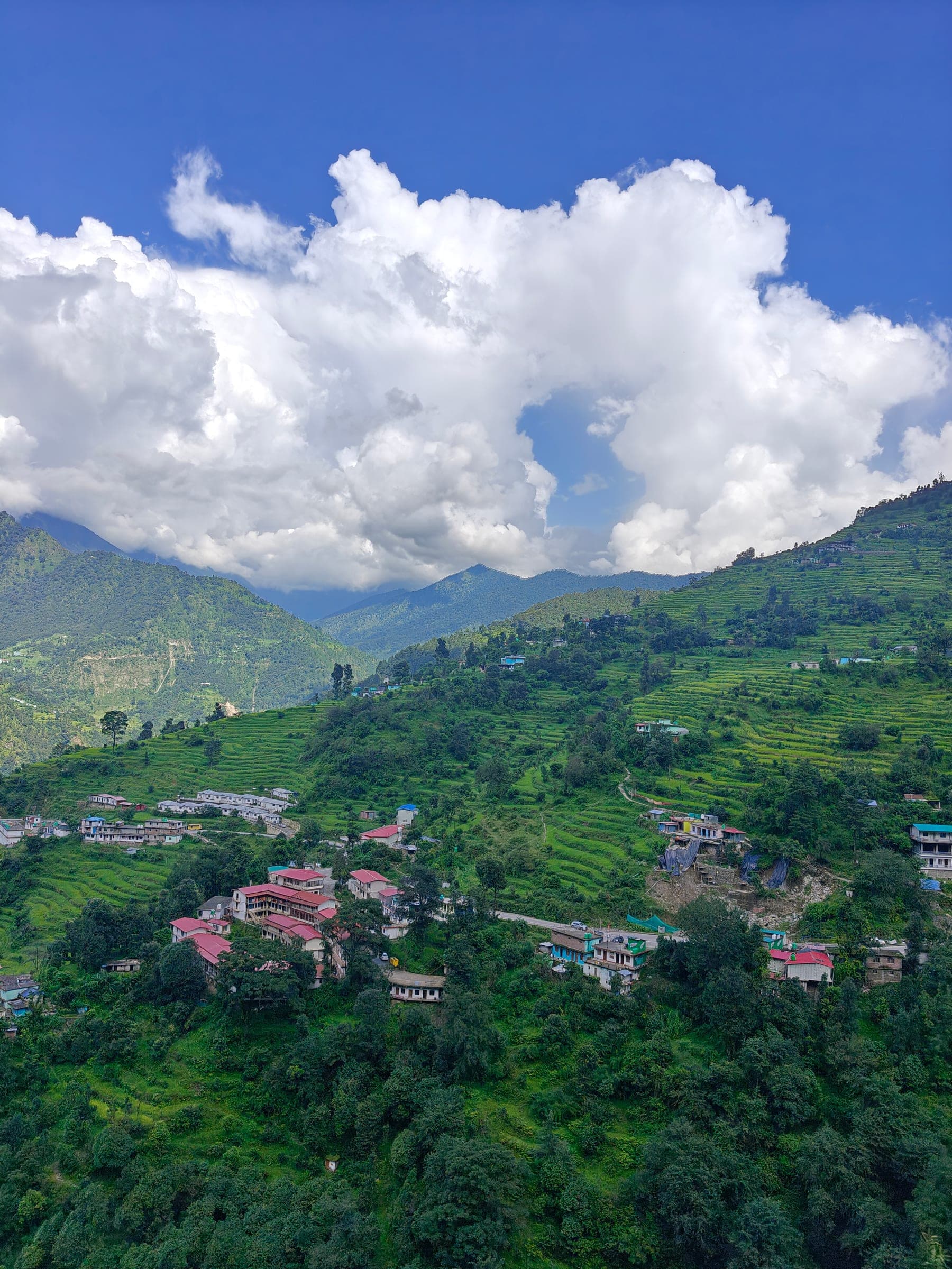 Terraced hillsides and a village of red-roofed houses under towering white clouds.